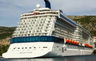 Celebrity Reflection cruise ship with white hull and blue stripe docked near a hillside coastline